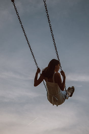 A young woman enjoying a care moment on a swing with a serene sky backdrop. HD phone wallpaper
