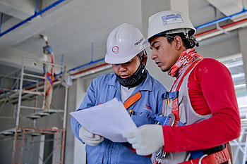 Two engineers in safety helmets reviewing construction plans at a worksite. HD wallpaper