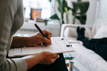 Therapist taking notes on clipboard during a session with a patient lying on a couch. HD wallpaper