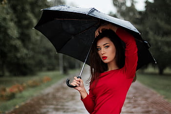 Chic woman in a red dress under an umbrella in the rain, showcasing fashion and elegance. HD wallpaper
