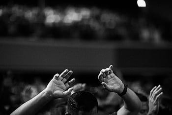 A black and white of hands raised in a crowd during a concert or religious gathering indoors. HD wallpaper