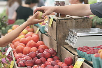 A customer exchanges an apple with a vendor at a vibrant farmers market. HD wallpaper