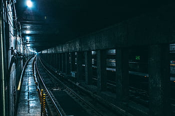A dark and atmospheric subway tunnel with moody lighting and train tracks extending into the distance. HD wallpaper