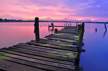 Peaceful sunset view over a wooden dock stretching into calm waters, vibrant sky colors. HD wallpaper