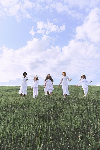 Five diverse women in white dresses running joyfully in a grassy field under a cloudy sky. HD phone wallpaper