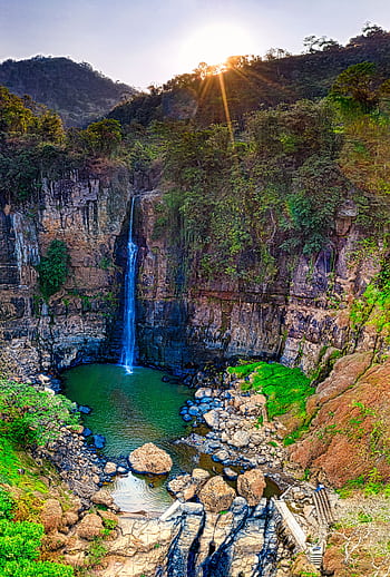 Breathtaking view of a tall waterfall in West Java's lush landscape, illuminated by morning sunrays. HD phone wallpaper