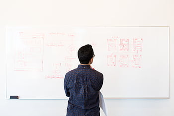 Man standing at a whiteboard planning UX design concepts in a modern office setting. HD wallpaper