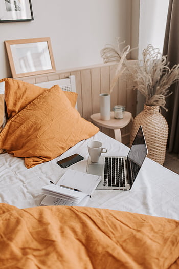 A comfortable work from home setup in a modern bedroom with laptop, coffee, and orange decor. HD phone wallpaper