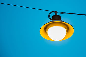 A striking yellow street light illuminating brightly against a blue sky, showcasing modern urban design. HD wallpaper