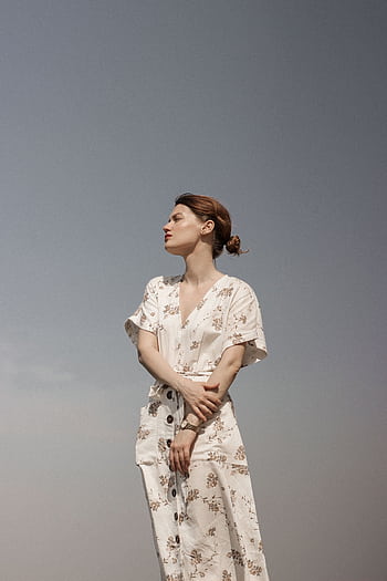 Portrait of a contemplative woman in a floral dress against a clear sky, exuding serenity and style. HD phone wallpaper