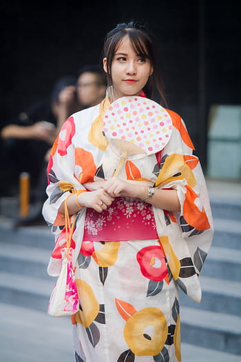 A young woman wearing a colorful floral kimono and holding a fan, embodying traditional Japanese fashion. HD phone wallpaper