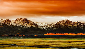 Scenic view of snow-capped mountains under a vibrant orange sky during sunset. HD wallpaper