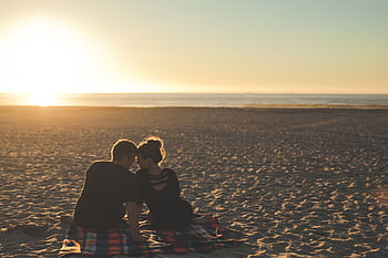 A couple enjoys sunset together on a sandy beach, capturing a moment of love and togetherness. HD wallpaper