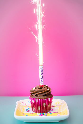 Colorful chocolate cupcake with a sparkling candle against a vibrant pink background. HD phone wallpaper