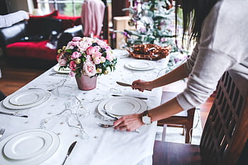 A woman sets a beautifully decorated dining table with flowers for a festive occasion indoors. HD wallpaper