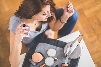 Young woman applying perfume with makeup essentials around her. HD wallpaper
