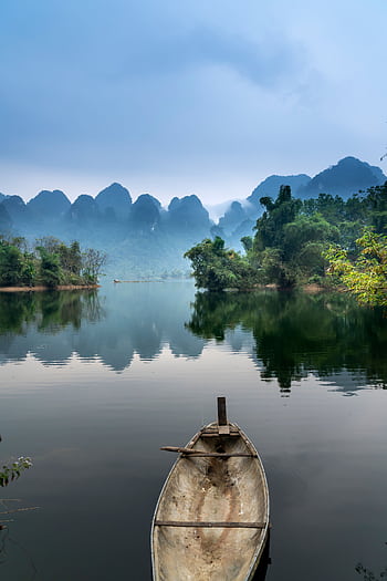 A tranquil river scene with a canoe, misty mountains, and lush greenery, perfect for nature lovers. HD phone wallpaper