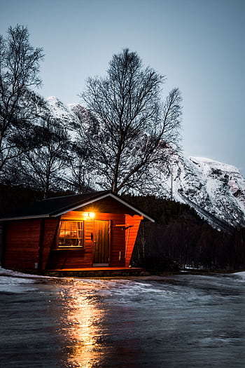 Charming cabin in Norway's winter landscape with snow-capped mountains and icy foreground. HD phone wallpaper