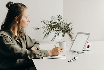 lancer writing notes in a minimalist home office with a white tablet, plant, and reading glasses. HD wallpaper