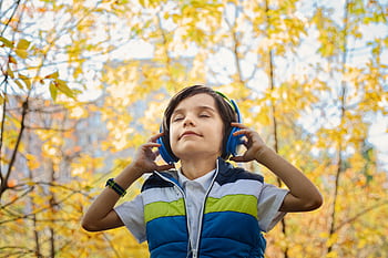 A young boy enjoys music through heads amidst colorful fall foliage. HD wallpaper