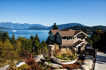 Scenic view of a charming house by the lake surrounded by mountains and lush greenery. HD wallpaper