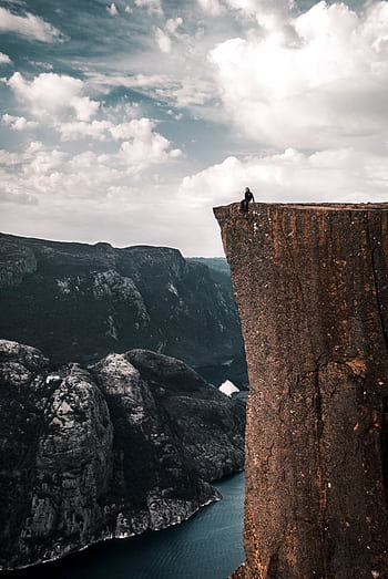A daring traveler sits on the edge of Preikestolen, overlooking breathtaking Norwegian fjords. HD phone wallpaper
