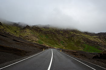 A foggy mountain road in Iceland, offering a serene travel scene with lush green hills. HD wallpaper