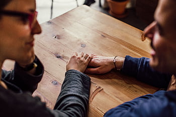 A couple shares a romantic moment holding hands across a wooden table indoors. HD wallpaper