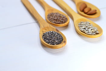 A variety of seeds and nuts in wooden spoons displayed on a white surface. HD wallpaper