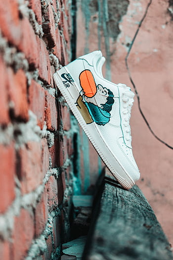 White Nike sneakers with cartoon design against a rough brick wall in urban setting. HD phone wallpaper