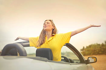 A cheerful woman in a yellow shirt enjoys dom on a sunny drive in a convertible. HD wallpaper