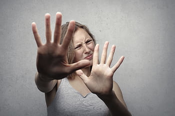 Portrait of a fearful woman in a gray tank top with hands pushed forward against a gray background. HD wallpaper