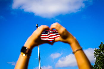 Hands form a heart shape around an American flag against a vibrant blue sky, symbolizing patriotism and dom. HD wallpaper