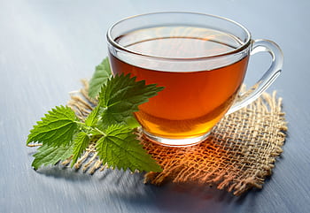 A close-up of herbal tea in a glass cup with fresh mint leaves on a table. HD wallpaper