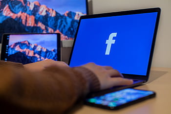 Laptop displaying Facebook at workspace with multiple devices, highlighting modern technology. HD wallpaper