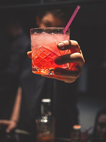 Close-up of a hand holding a vibrant cocktail with ice and a straw, perfect for nightlife themes. HD phone wallpaper