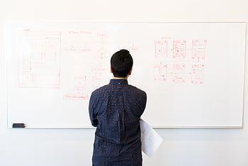 Man analyzing design flowchart on whiteboard in a professional office setting. HD wallpaper