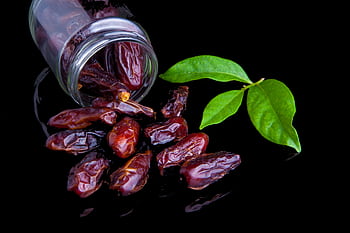 Delicious fresh dates with leaves on a black background, showcasing healthy eating. HD wallpaper