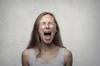 Young woman screaming with emotion, showing braces, against a gray backdrop. HD wallpaper