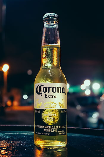 A bottle of Corona beer stands illuminated against a blurred night city background, creating a vibrant urban atmosphere. HD phone wallpaper