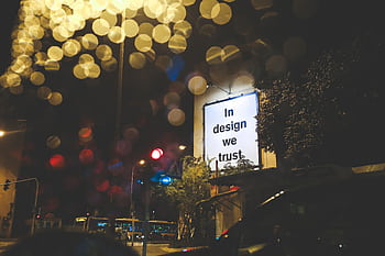 A city street at night featuring an illuminated billboard with the phrase 'In design we trust.' HD wallpaper