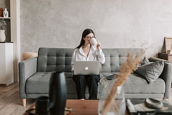 Woman sipping coffee while working on a laptop in a cozy home setting, highlighting remote work lifestyle. HD wallpaper