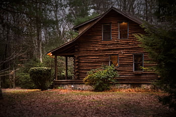 A cozy log cabin surrounded by autumn trees, showcasing warm lighting and tranquil nature. HD wallpaper