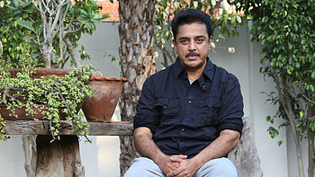 Actor Kamal Hassan Is Wearing Black Shirt And White Pant Sitting In Green Plants Background Boys HD wallpaper