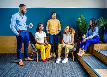 A diverse group of five professionals engaging in a casual indoor meeting, smiling and talking. HD wallpaper