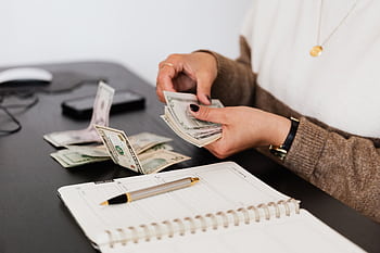 Close-up of person counting cash with notepad on desk, indicating financial tasks. HD wallpaper