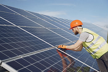 A solar technician in protective gear installs solar panels on a sunny day, highlighting renewable energy work. HD wallpaper