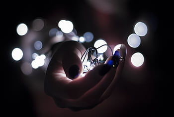 Close-up of a hand holding glowing string lights with a bokeh effect, creating a festive atmosphere. HD wallpaper