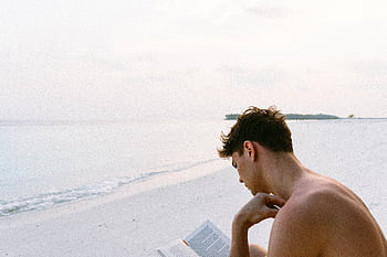 A man enjoys reading a book on a serene Maldives beach, capturing the essence of relaxation. HD wallpaper