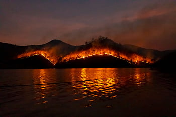 Dramatic wildfire in Thailand with blazing mountains reflecting in the dark waters. HD wallpaper